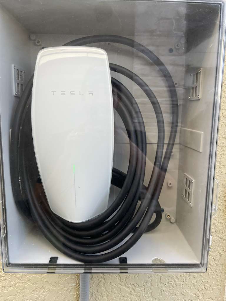Tesla Universal Wall Connector behind a clear weather-resistant cover at an Airbnb property